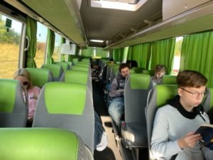 Schüler und Lehrer sitzen im Bus und beschäftigen sich mit Lesen, Gesprächen und Musik hören.